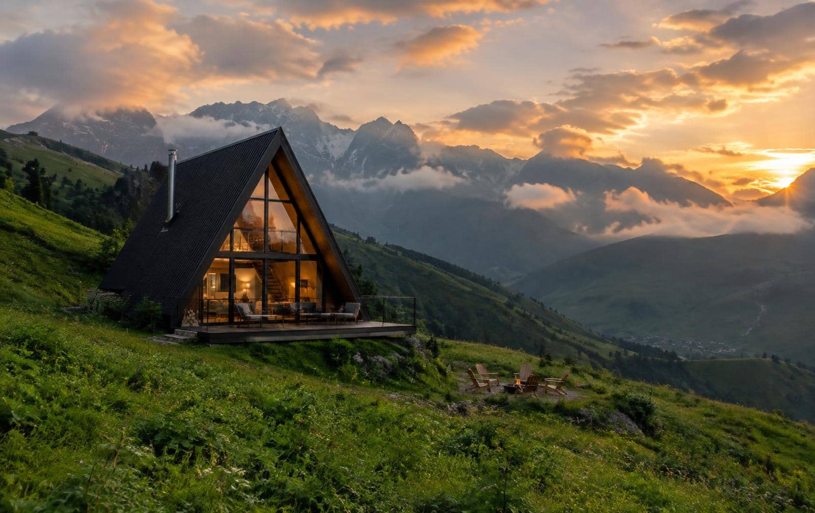 Black A-frame cottage with a glass facade on a mountain slope in Georgia at sunset